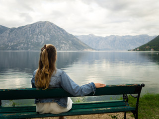 A girl sitting on a bench admiring еhe view of the Kotor Bay.  Montenegro autumn 2019