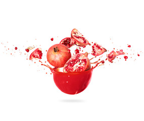 Whole and chopped pomegranate in splashes of fresh juice on a white background © Krafla