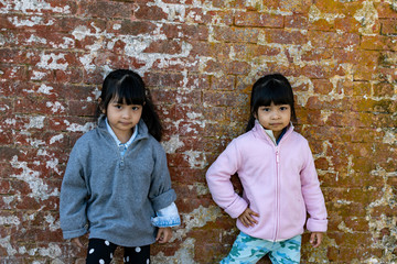 Asian identical female twins child wearing jacket during cold weather and standing on an old brick wall background