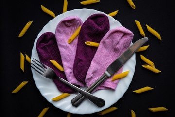 Creative composition of colorful pink and dark red socks arranged on a white plate with fork and knife on dark black background