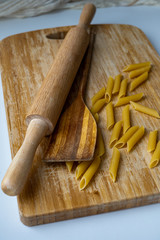 Uncooked penne spaghetti with wooden rolling pin and wooden spatula on wooden cutting board