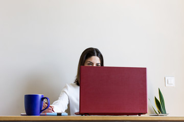 Front view of casual woman working from home during confinement season, due to Covid. Telecommuting. With a cup of coffee on the table.