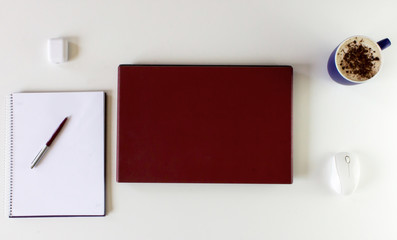 White desk with red computer, cup of coffee, note book and a pencil.