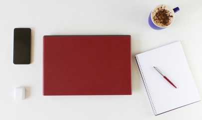 white desk with red computer, cup of coffee, note book and a pencil.