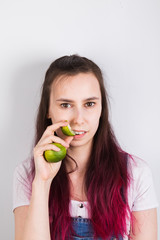 Young girl with pink hair eats lime on grey background
