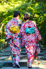Japan Destination. Two Young Female Geishas in Traditional Japanese Floral Silk Kimono Going Uphill in Green Forest in Kyoto City,  Japan.