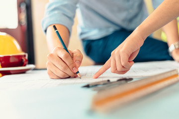 engineers holding a pen pointing to a building and  drawing outlay construction plan as guide for...