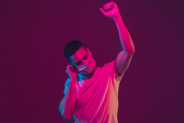 Listen to music, dancing. Caucasian man's portrait isolated on pink-purple studio background in neon light. Male model with devices. Concept of human emotions, facial expression, sales, ad.