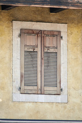 Fototapeta na wymiar Italian window on the yellow old paint wall facade with closed old wooden classic shutters