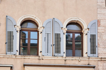 Two Italian windows on the pink wall facade with open wooden light grey color classic shutters