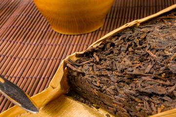Chinese pressed PU-erh tea in bamboo leaf packaging and tea knife on a bamboo Mat, close-up, macro