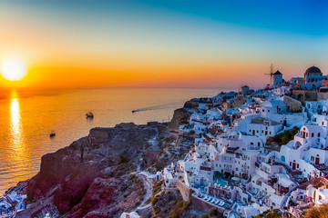 Fototapeta premium Greek Traveling Concepts. Sailing Boats Near Caldera Volcanic Slopes of Santorini Oia or Ia Village in Greece Enjoying Sunset.