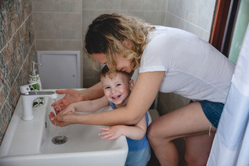 mom helps her little son wash his hands at home over the sink