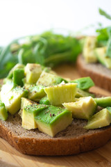 Healthy  breakfast toasted rye bread with avocado, arugula, lemon juice, salt and pepper on a wooden plate