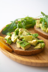 Healthy  breakfast toasted rye bread with avocado, arugula, lemon juice, salt and pepper on a wooden plate
