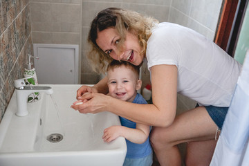 mom helps her little son wash his hands at home over the sink