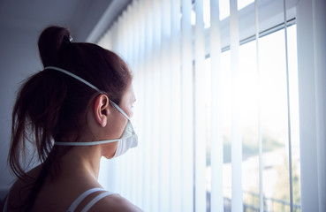 Young woman looking out of window wearing protective face mask.