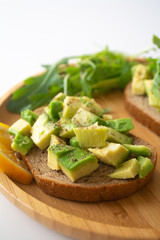 Healthy  breakfast toasted rye bread with avocado, arugula, lemon juice, salt and pepper on a wooden plate