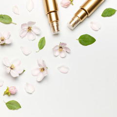 Cosmetics springtime Concept. Cosmetics, spring white flowers green leaves on light background. Cosmetic mock up gold bottles. Flat lay top view copy space. Branding products, beauty background