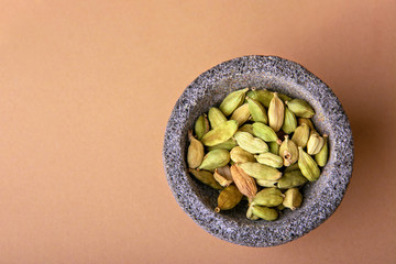 Dried green cardamom seeds in a stone mortar on a brown background. Alternative medicine and therapy