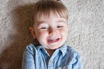 Fototapeta premium Top view of cheerful little kid smiling on the carpet floor at home.