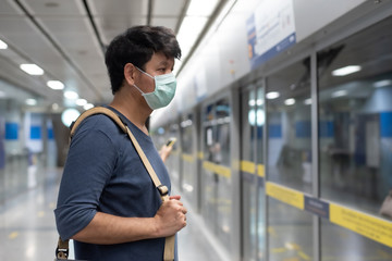 Asian man wear surgical face mask carrying  shoulder bag waiting for the train in a subway, side...
