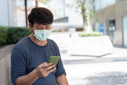 Asian man wear surgical face mask looking at smart phone in the city, coronavirus,covid19