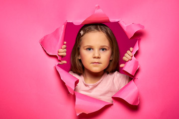 Beauty portrait of teenage girl peeking out from behind pink torn paper.Through paper.Girl through hole in paper.