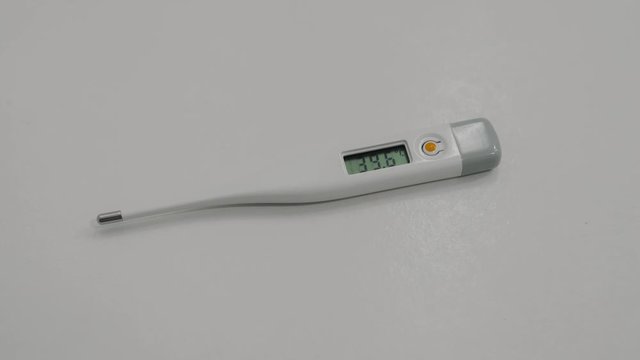 Close up shot. The men's hand put the medical digital thermometer with hight body temperature 39 degrees on white background, Covid-19 and the epidemic of infection, 4k
