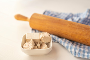 close up detail of fresh yeast cube  on a white background in a white porcelain dish with rollingpin  