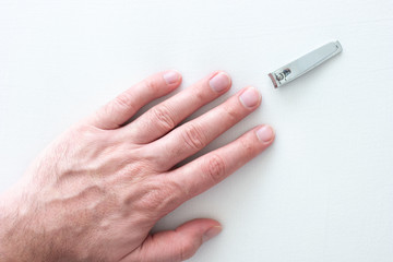 Caucasian male straight extended hand and uncut long nails and nail clipper on white surface top view close up shot