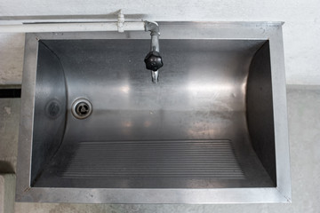 Large silver metal washing sink and piping inside a common use laundry room inside shot top view