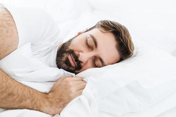 Fototapeta na wymiar Image of young unshaven caucasian man sleeping alone in bed at home
