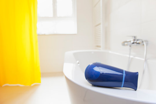 Hair dryer lying on a bathtub in a bright bathroom danger of electric shock