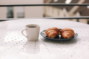 Coffee cup and fresh baked french croissants in blue plate on white background. Breakfast.