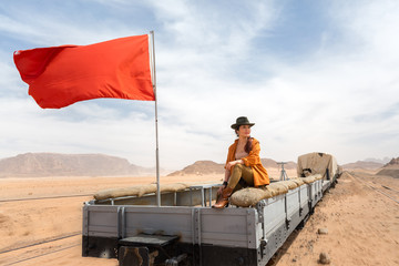 A cowboy girl walks on the sand next to a wooden open carriage of a vintage train in the Wadi Rum desert
