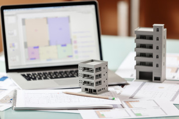 Close up of a house model standing over apartment plans in front of a laptop in a construction bureau.