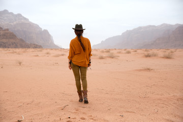 A girl in a cowboy hat and boots walks on the sand in the Wadi Rum desert in Jordan