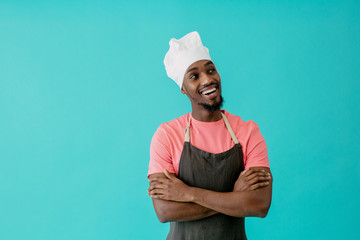 Portrait of an excited young male chef with arms crossed and mouth open looking to side, against blue studio background
