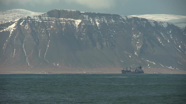 Distant cargo ship sailing under towering mountains Iceland