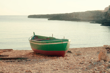 Naklejka premium An abandoned fishing boat on the shoreline, waiting for the sailors to begin another workday. Warm morning with bright shiny lights. 