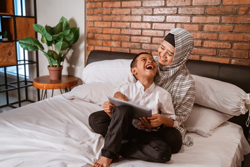 muslim family mother using tablet on the bed with son