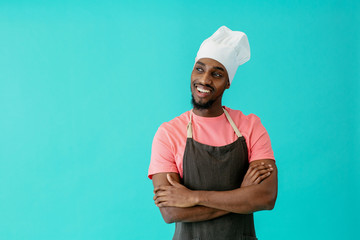 Portrait of a friendly young male chef with arms crossed and looking to side, against blue studio background