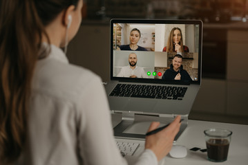 A Back view of a woman working remotely in a video conference with her colleagues during an online meeting. Partners in a video call. Multiethnic business team having a discussion in an online meeting