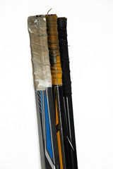 Hockey sticks for playing with a puck on a white background stand in a row, the handles are rewound...