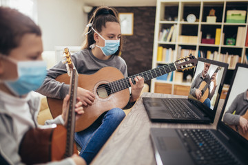 Fototapeta na wymiar Boy and girl, wear protective masks, playing acoustic guitar and watching online course on laptop while practicing at home. Online training, online classes.