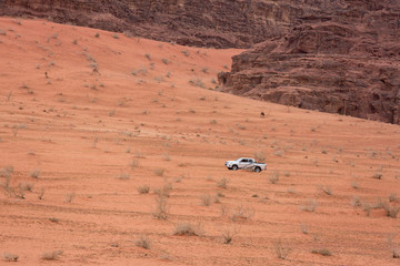 Fototapeta na wymiar The car rides on a sandy slope amid the rocky mountains of the Wadi Rum desert. Mars is a lifeless red landscape