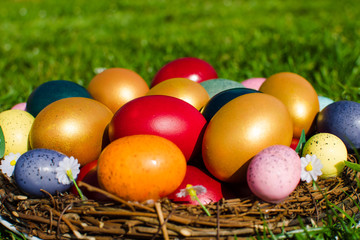 Easter eggs pictured in a wooden basket on green grass.