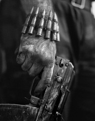 Fototapeta na wymiar Dirty rebel hand with a machine gun and a bracelet with machine-gun cartridges.