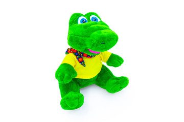 Plush soft, green, children's crocodile toy isolated on a white background with shadow reflection. Front view on the right. The beautiful doll is dressed in a yellow t-shirt and a colorful scarf.